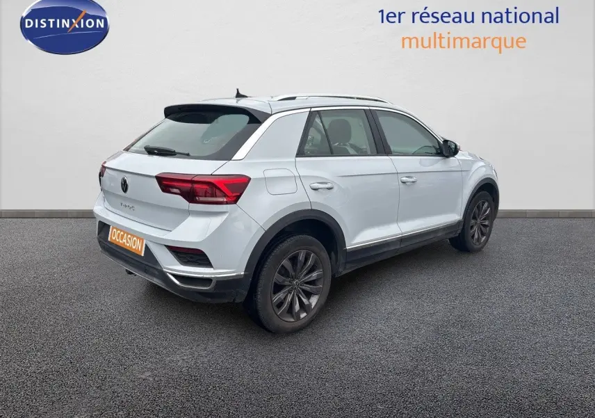 Volkswagen T-Roc blanc argenté vu en 3/4 arrière droit, avec jantes foncées et toit ouvrant visible.