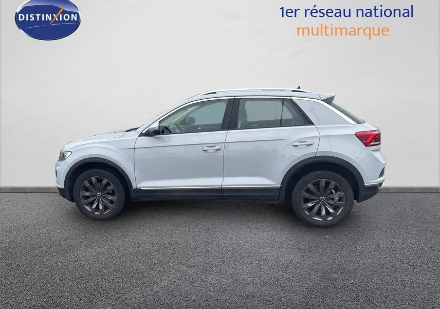 Profil côté gauche d'un Volkswagen T-Roc blanc argenté 2021 avec jantes foncées et toit ouvrant visible.