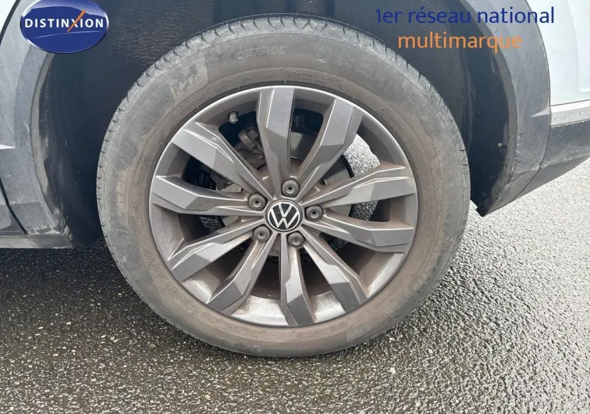 Gros plan sur la roue avant gauche d'un Volkswagen T-Roc blanc argent avec jante alliage grise et logo VW central.