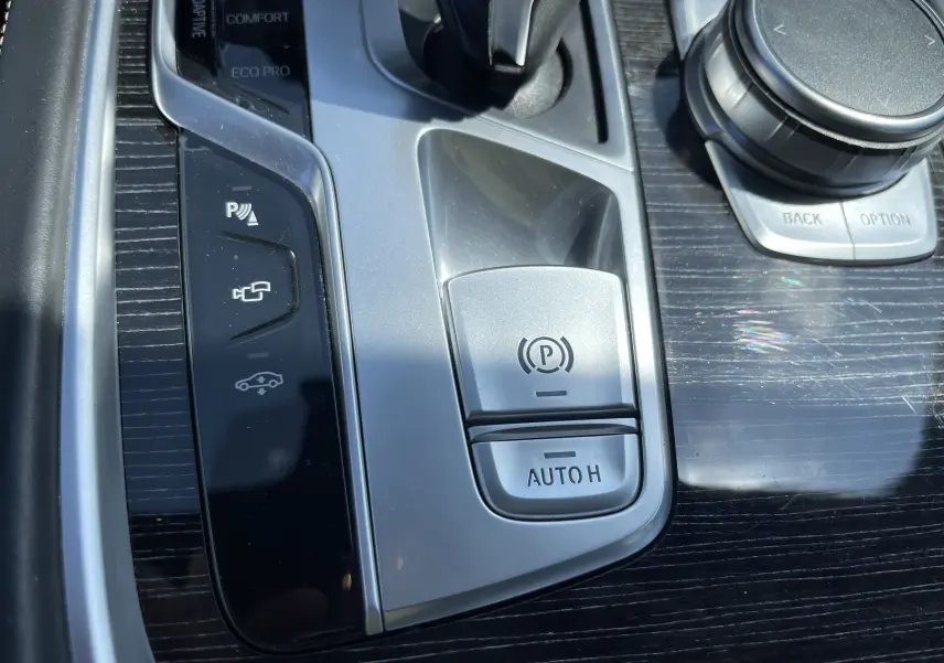Gros plan sur la console centrale noire et argentée d'une BMW Série 7 G11, avec boutons de frein à main et modes de conduite.