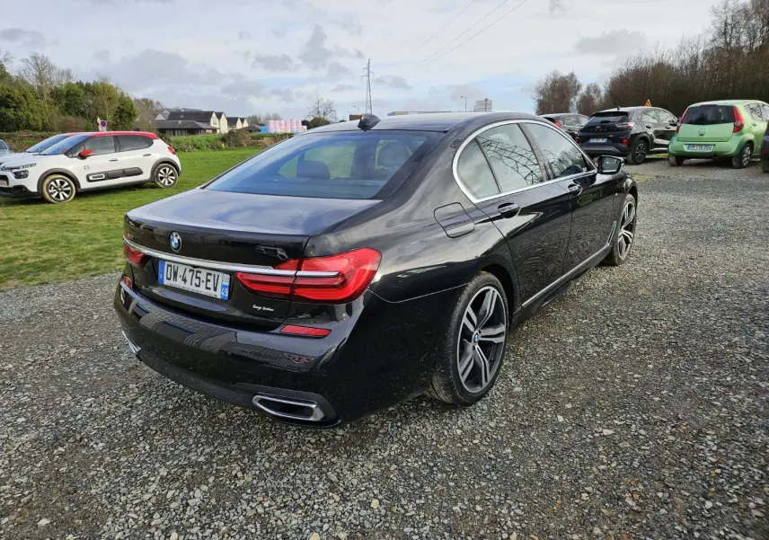 BMW Série 7 G11 noire vue en 3/4 arrière droit sur un parking, avec jantes M Sport et feux LED distinctifs.