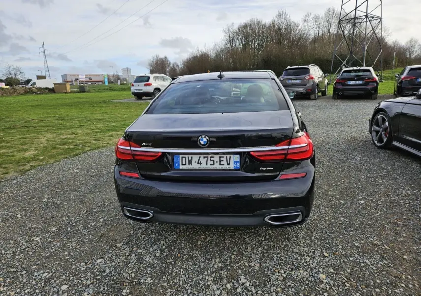 Vue arrière d'une BMW Série 7 G11 noire avec feux LED et double sortie d'échappement dans un parking extérieur.
