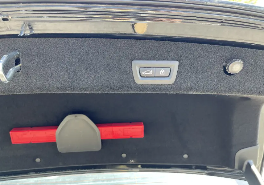 Intérieur du coffre de la BMW Série 7 noire, vue du hayon ouvert avec bouton de fermeture électrique et triangle de signalisation rouge.