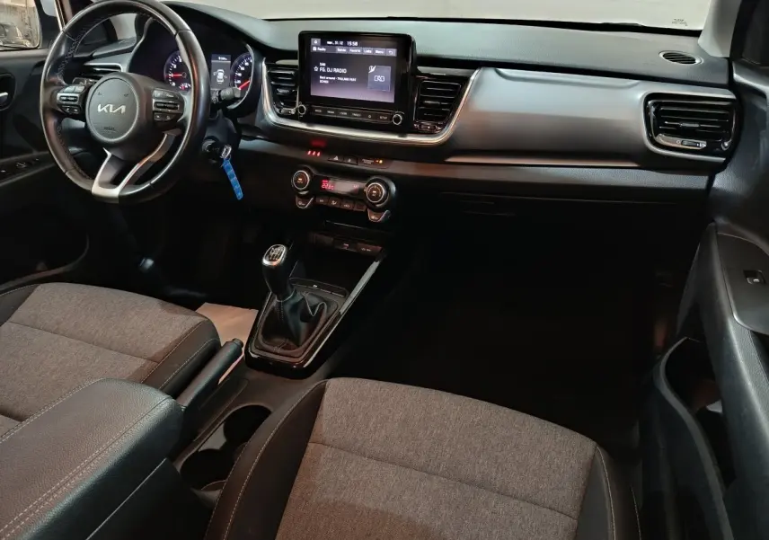 Vue intérieure côté conducteur du tableau de bord et console centrale du KIA Stonic gris clair avec boîte manuelle et écran tactile.