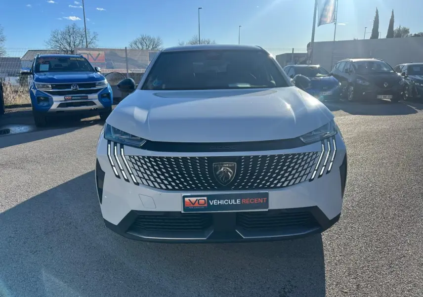 Vue avant d'un Peugeot 3008 Hybrid blanc de 2025 avec calandre distinctive et feux LED verticaux allumés.