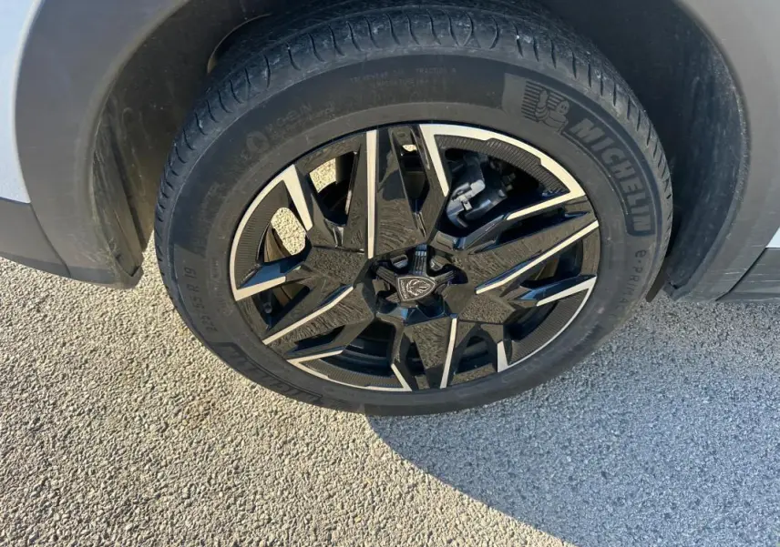 Gros plan sur la jante alliage 19 pouces noire et argentée du Peugeot 3008 Hybrid blanc, côté gauche arrière.