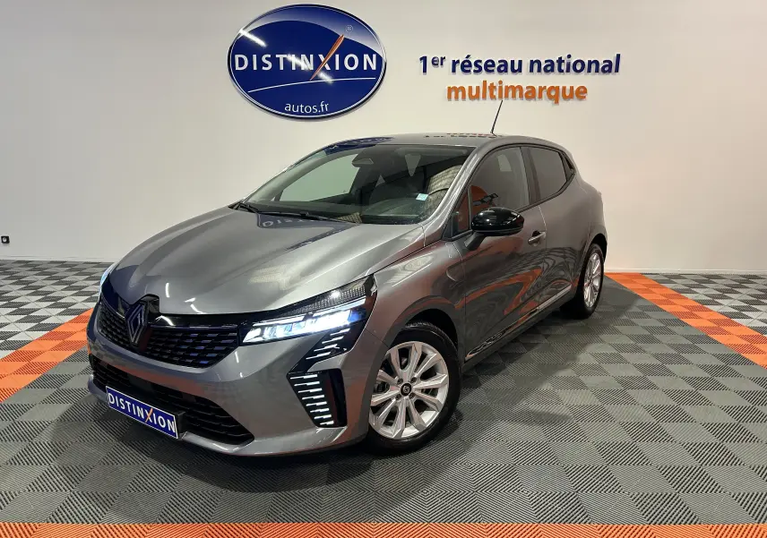 Renault Clio V gris schiste métal vue 3/4 avant droit avec phares LED allumés dans un showroom.