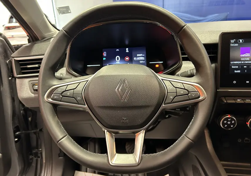 Vue rapprochée du volant cuir noir de la Renault Clio V 2025 avec tableau de bord digital et commandes intégrées.
