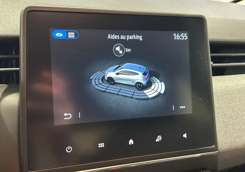 Écran tactile intérieur montrant l'aide au parking d'une Renault Clio V gris schiste en vue 3/4 arrière.