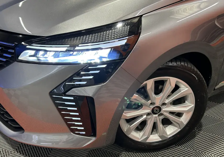 Gros plan sur l’avant droit gris schiste métal de la Renault Clio V avec phare LED allumé et jante alliage visible.