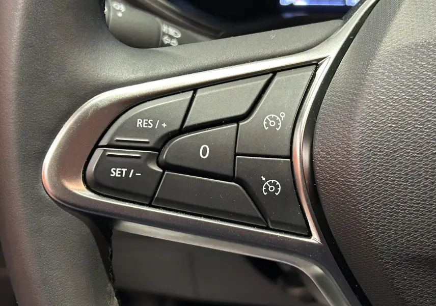 Gros plan sur les commandes de régulateur de vitesse noires avec contour argenté sur le volant d’une Renault Clio V gris schiste.