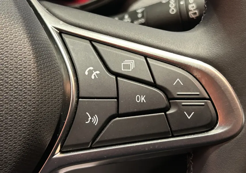 Gros plan sur les commandes multifonctions noires du volant d’une Renault Clio V, finition tissu noir.