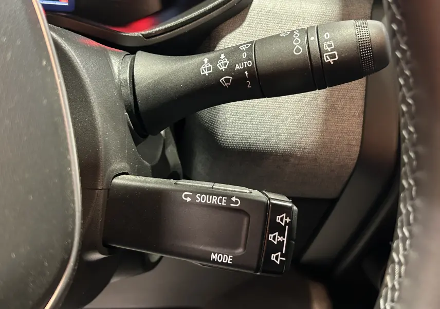 Gros plan sur les commandes au volant côté gauche de la Renault Clio V gris schiste, avec commandes de phares et audio.