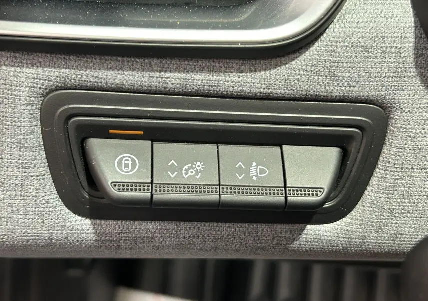 Gros plan sur les boutons de réglage d’éclairage et verrouillage intérieur de la Renault Clio V, tissu gris visible.