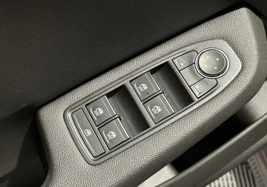 Gros plan sur les commandes des vitres électriques et rétroviseurs côté conducteur d'une Renault Clio V gris schiste.