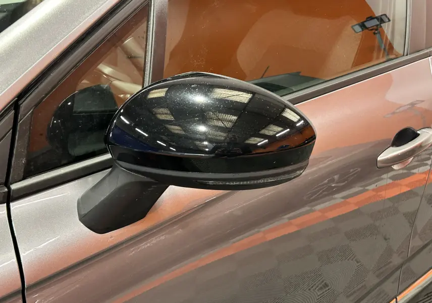 Gros plan sur le rétroviseur noir côté gauche d'une Renault Clio V gris schiste métal, avec reflet intérieur visible.