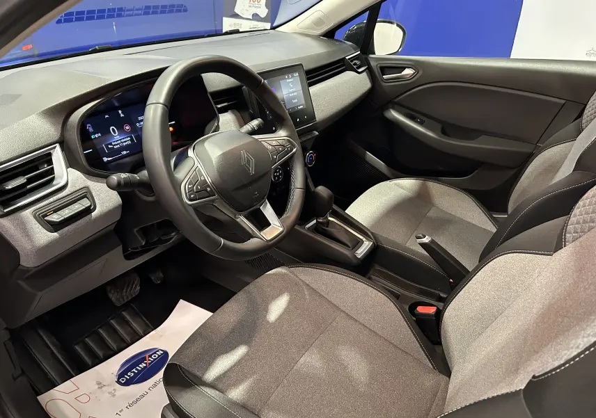 Vue intérieure côté conducteur de la Renault Clio V 2025, avec tableau de bord numérique et sellerie tissu gris clair.