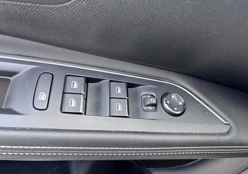 Gros plan sur les commandes de lève-vitres et réglage des rétroviseurs côté conducteur d’un Peugeot 5008 blanc.