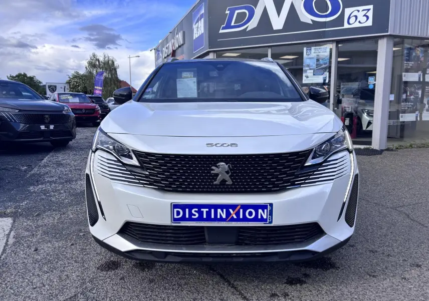 Vue avant d'un Peugeot 5008 blanc 2022 avec calandre noire et phares LED, devant un concessionnaire Distinxion.