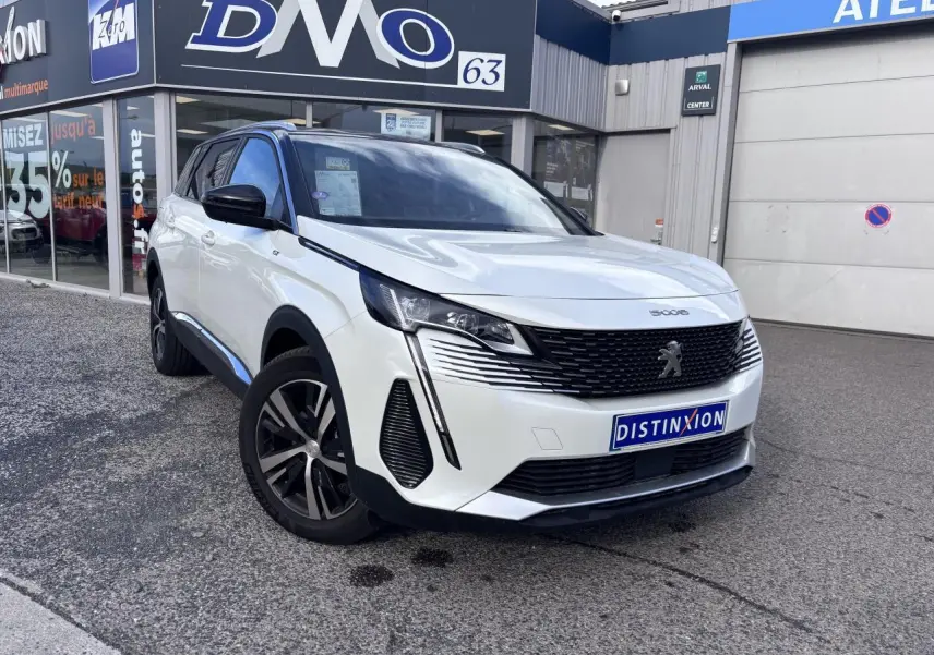 Peugeot 5008 blanc en 3/4 avant droit, avec calandre noire et jantes alliage distinctives, devant un garage.