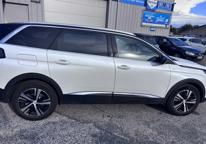 Profil côté droit d'un Peugeot 5008 blanc 2022 GT avec jantes alliage noires et vitres teintées.