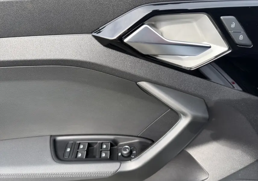 Détail de la porte côté conducteur de l'Audi A1 Sportback 2025 blanche, avec commandes des vitres et poignée argentée.