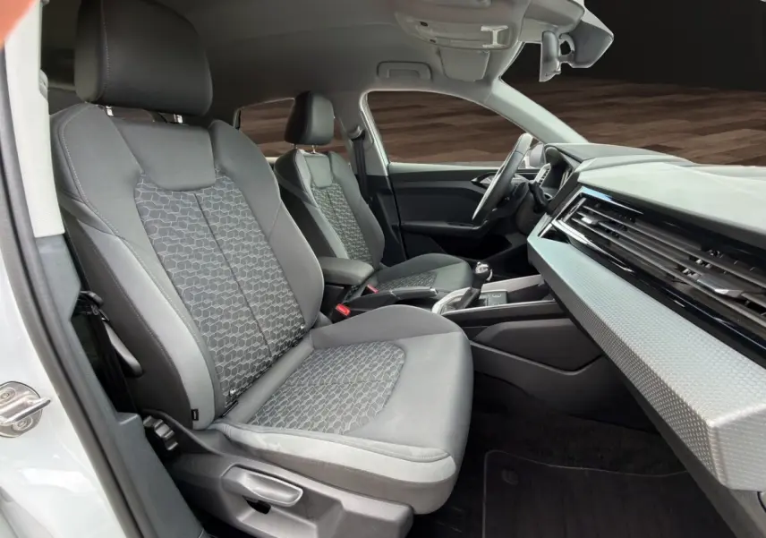 Vue intérieure côté conducteur de l'Audi A1 Sportback 2025 avec sièges gris et tableau de bord moderne blanc texturé.