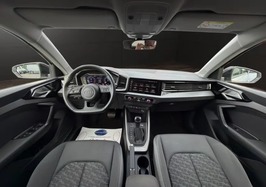 Vue intérieure avant de l'Audi A1 Sportback 2025 avec tableau de bord numérique et sièges gris foncé.