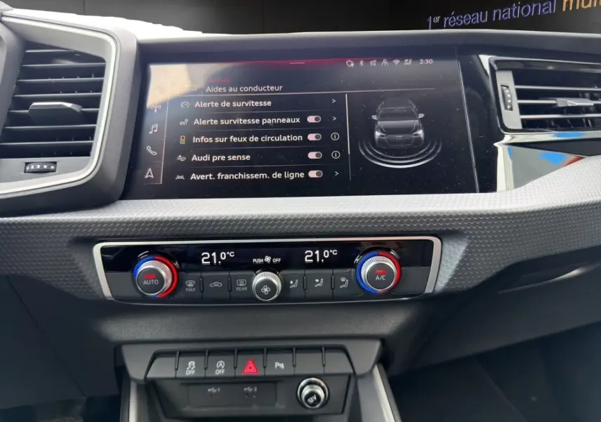 Vue rapprochée du tableau de bord de l'Audi A1 Sportback 2025 blanc, avec écran tactile et commandes climatisation digitales.