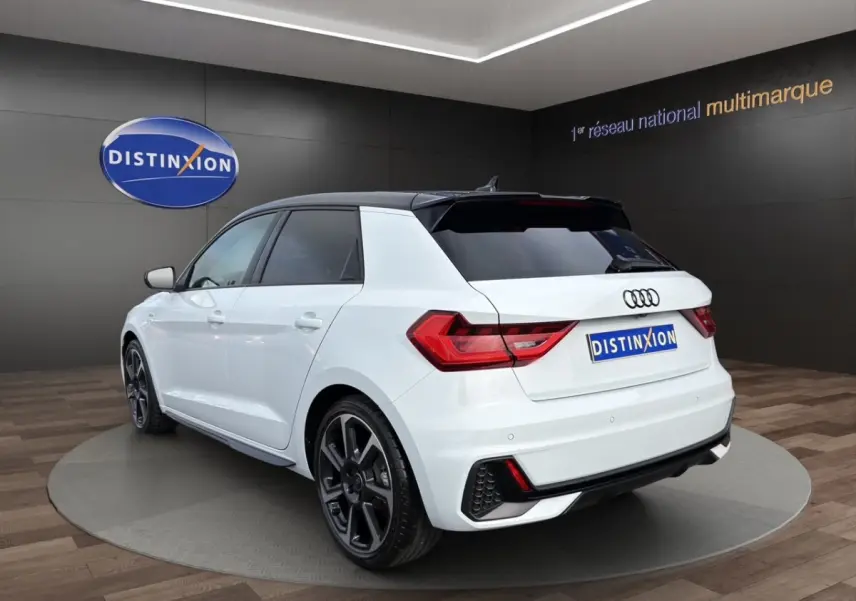 Audi A1 Sportback blanc vue 3/4 arrière droit en intérieur avec toit noir et jantes noires distinctives.