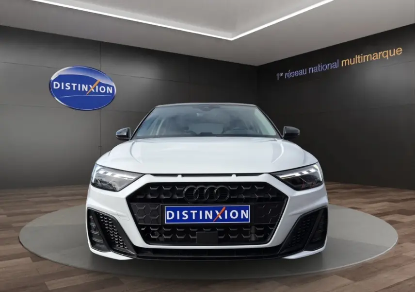 Vue frontale d'une Audi A1 Sportback blanche 2025 avec calandre noire et phares LED, en showroom Distinxion.