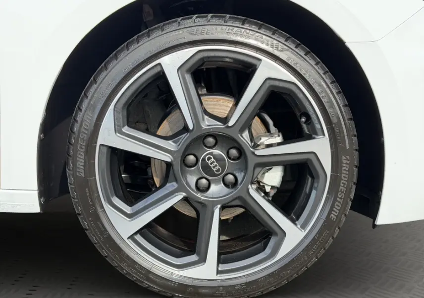 Gros plan sur la roue avant droite d'une Audi A1 Sportback blanche, jante alliage gris foncé à design moderne.