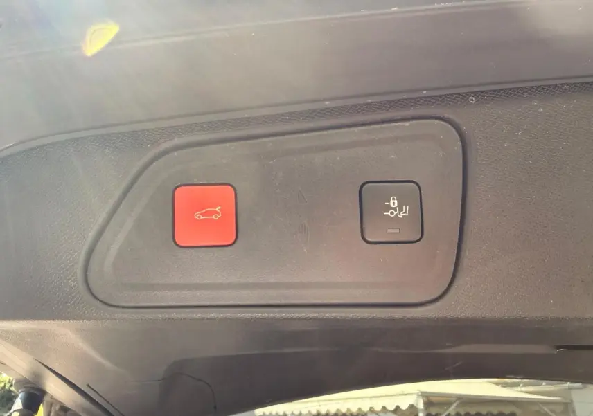 Gros plan sur les boutons d'ouverture et de verrouillage du hayon du Peugeot 3008 gris platinium, intérieur du coffre.