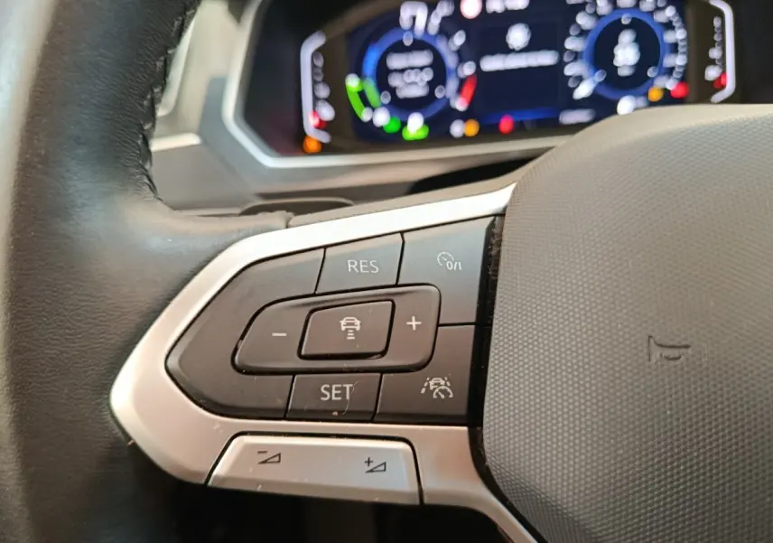 Gros plan sur le volant noir du Volkswagen Tiguan 2022 avec commandes de régulateur adaptatif et tableau de bord numérique flou.