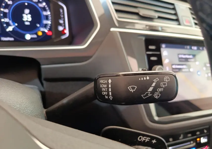 Gros plan sur la commande des essuie-glaces dans l’habitacle du Volkswagen Tiguan noir, avec tableau de bord numérique en arrière-plan.
