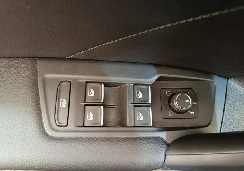 Gros plan sur les commandes de lève-vitres et réglage des rétroviseurs côté conducteur d’un Volkswagen Tiguan noir.