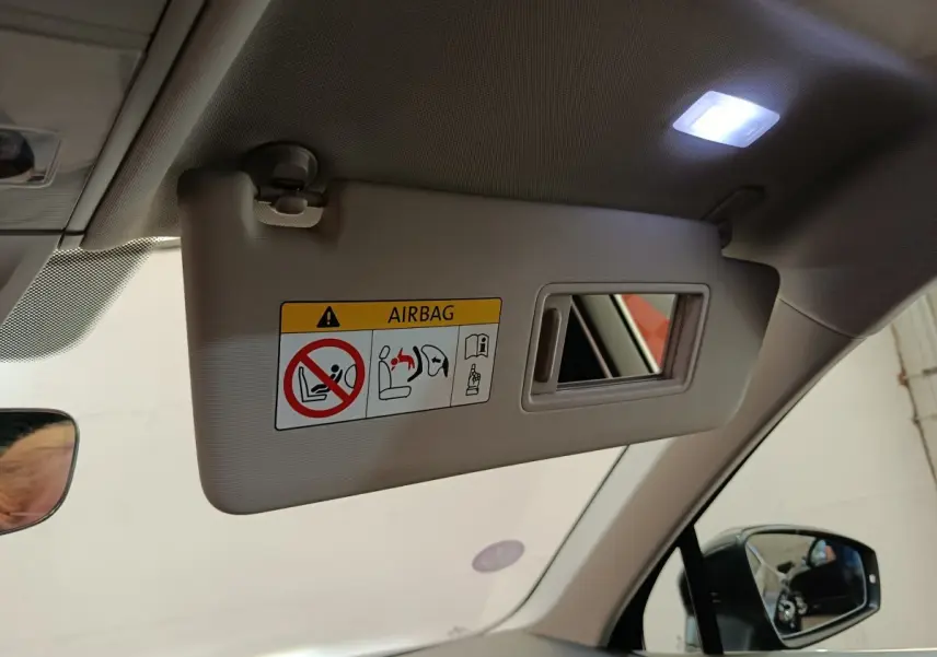 Détail intérieur du pare-soleil côté conducteur avec miroir et avertissement airbag dans un Volkswagen Tiguan noir.