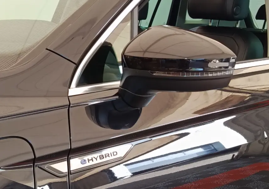 Gros plan sur le rétroviseur droit et l’inscription eHybrid d’un Volkswagen Tiguan noir brillant.