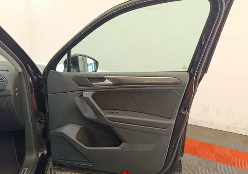 Porte avant gauche ouverte d’un Volkswagen Tiguan noir, intérieur avec garniture noire et insert décoratif gris.