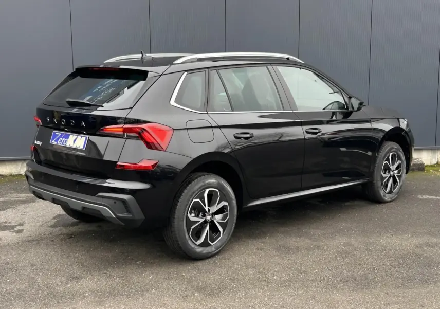 Vue 3/4 arrière droite d'un Skoda Kamiq noir Magic avec jantes alliage et baguettes chromées sur fond urbain.