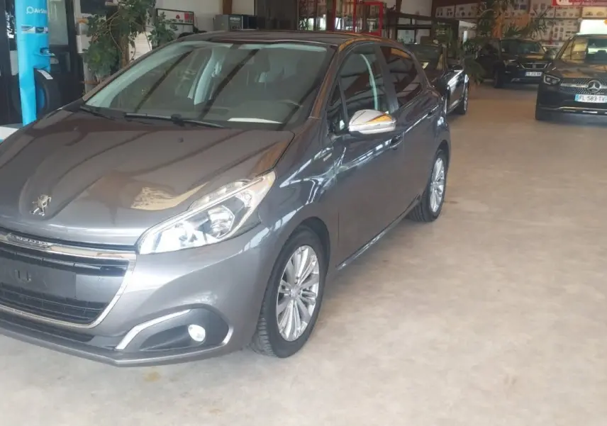 Peugeot 208 gris métal vue 3/4 avant droit dans un showroom avec plusieurs autres véhicules en arrière-plan.