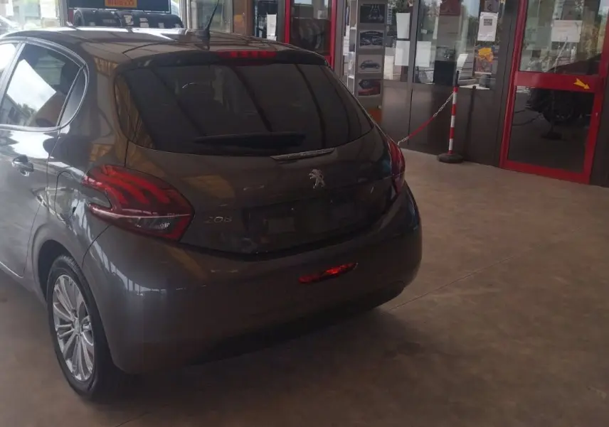 Peugeot 208 gris métal vue 3/4 arrière droit dans un showroom, avec feux arrière distinctifs et jantes alliage.