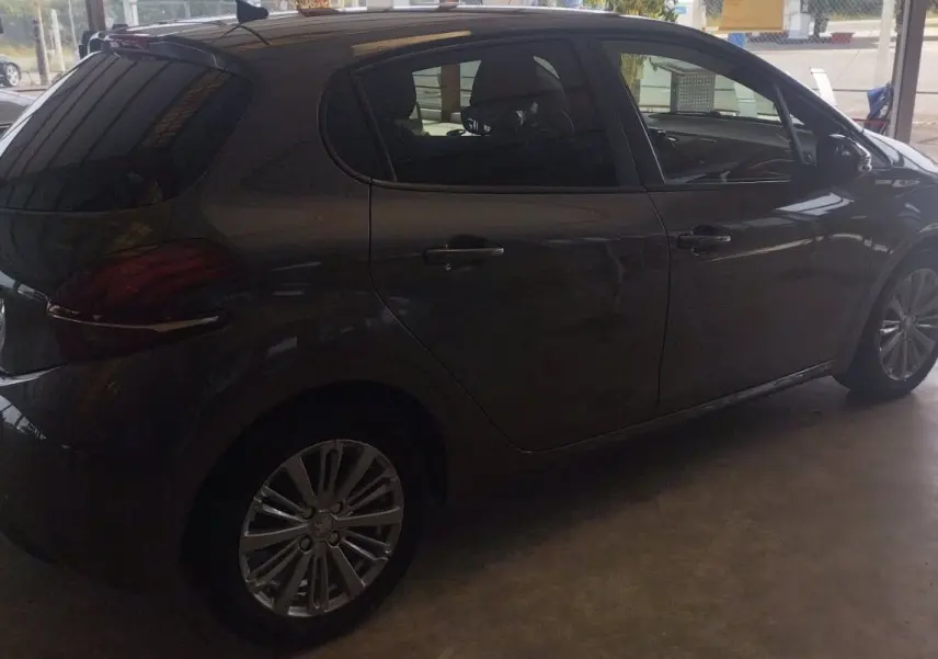 Peugeot 208 gris métal vue de profil côté droit dans un garage, mettant en valeur ses jantes alliage et vitres teintées.