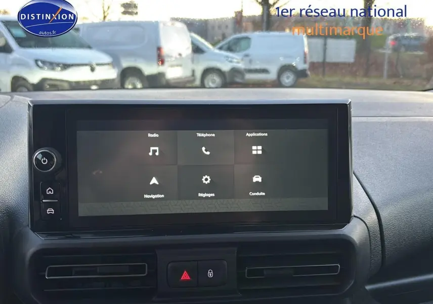 Vue intérieure centrée sur l'écran tactile du tableau de bord du Citroën Berlingo Fourgon blanc, avec vue floue sur l'extérieur.