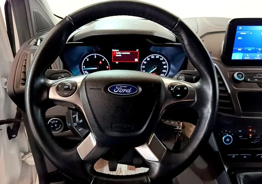 Vue intérieure centrée sur le volant noir Ford du Transit Fourgon blanc avec tableau de bord et écran tactile.