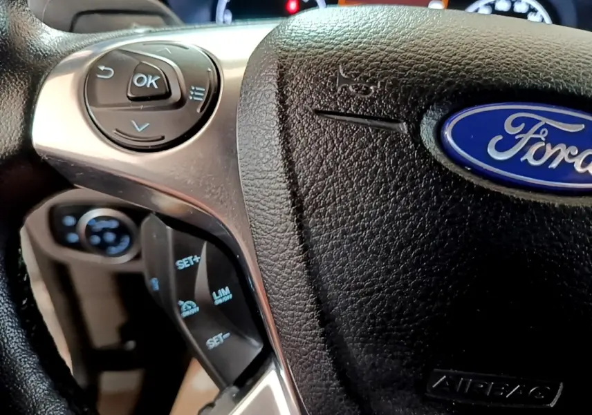 Gros plan sur le volant multifonctions noir du Ford Transit Fourgon blanc, avec commandes de régulateur de vitesse visibles.