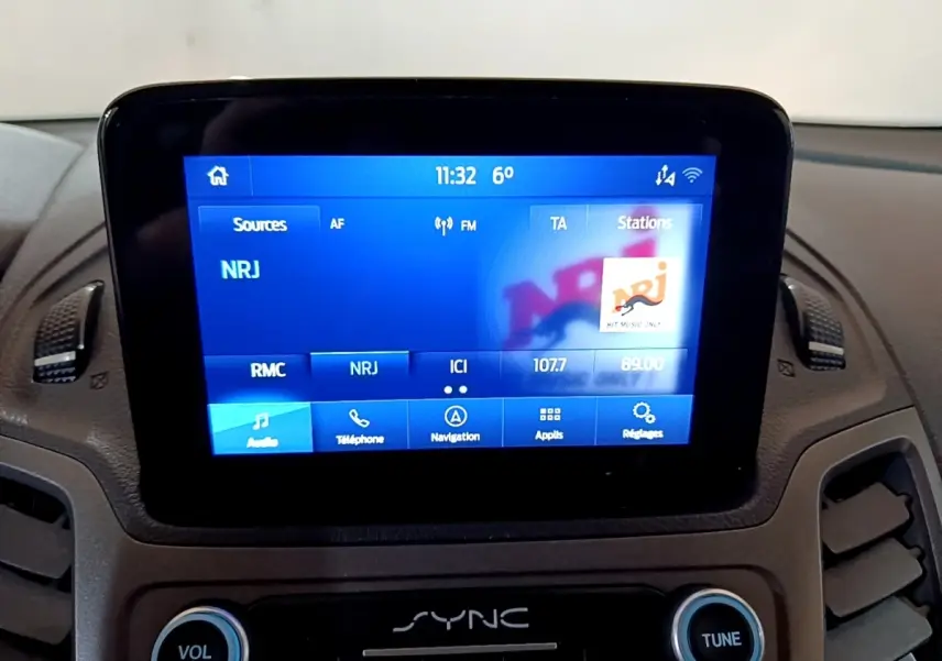 Écran tactile central du tableau de bord du Ford Transit Fourgon blanc, affichant la radio NRJ à 11h32.