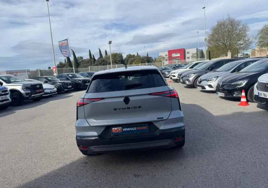 Vue arrière d'une Renault SYMBIOZ gris clair 2025 avec feux LED effilés et logo central noir sur parking.