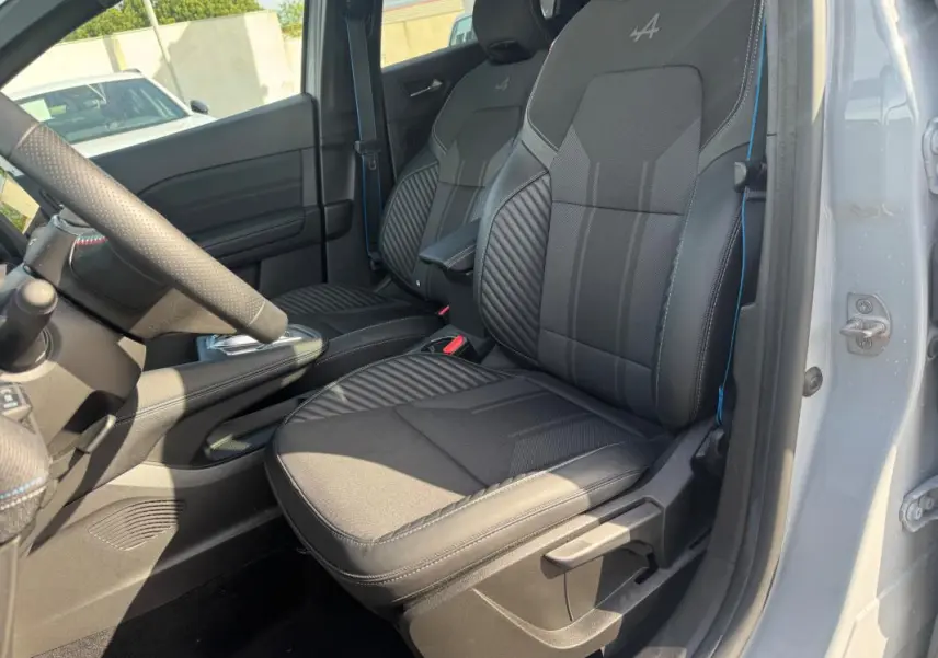 Vue intérieure côté conducteur du Renault Symbioz gris clair, mettant en valeur les sièges noirs avec logo Alpine brodé.