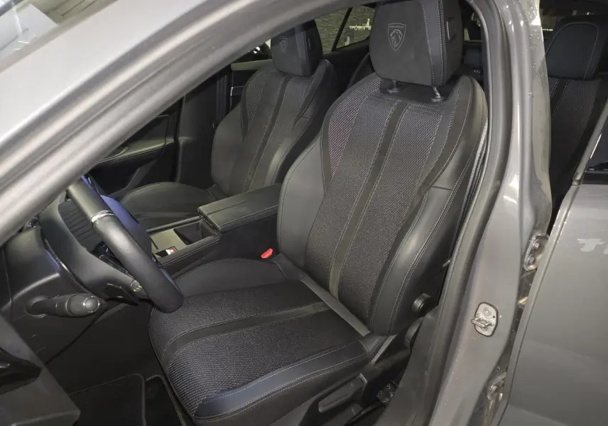 Vue intérieure côté conducteur de la Peugeot 408 gris Selenium, sièges tri-matières avec logo Peugeot brodé sur les appuis-tête.